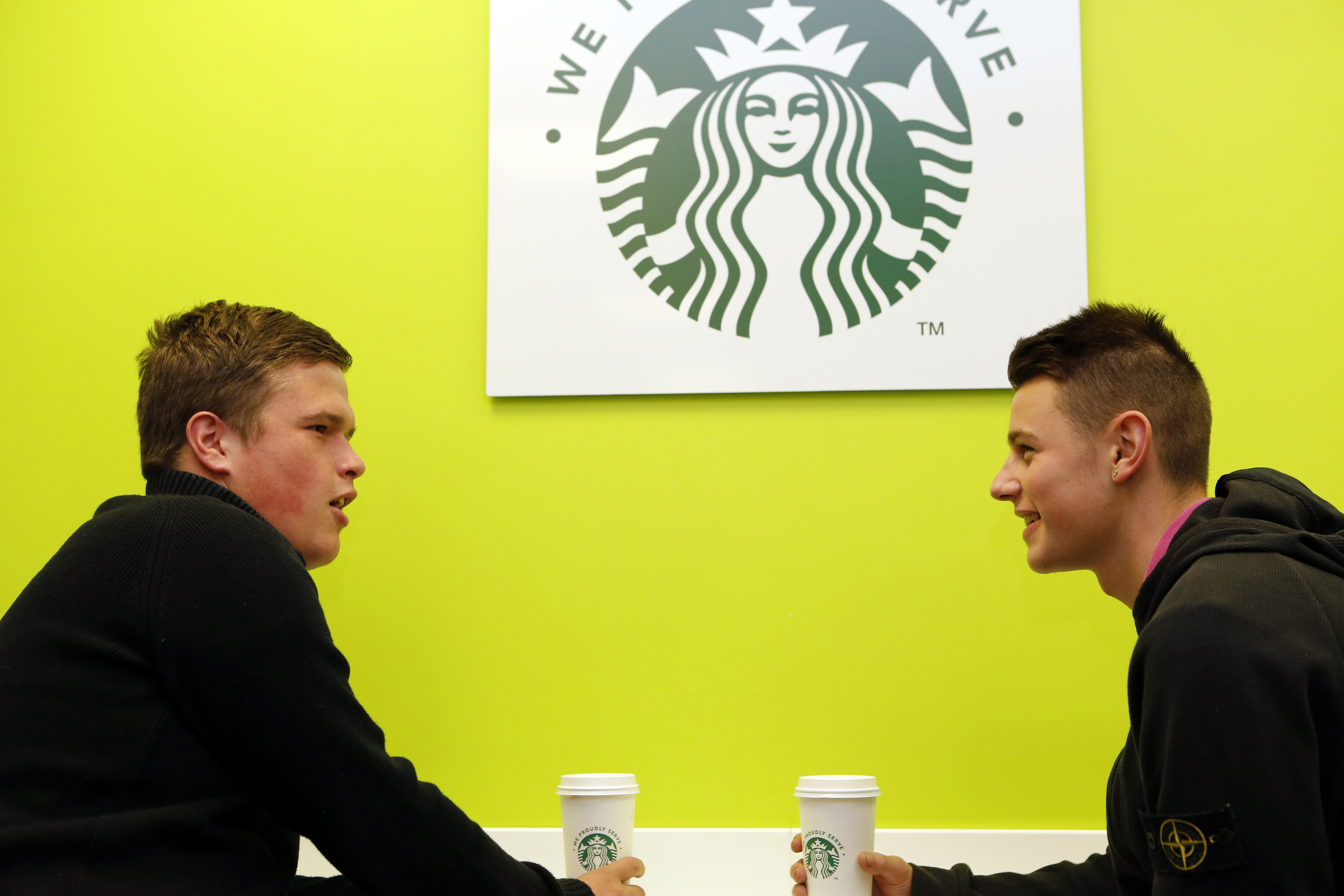 Image showing two students with Starbucks logo cup sitting beneath the Starbucks wall logo